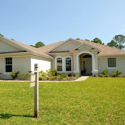 Beautiful suburban house with lush lawn, showcasing a for sale sign under a clear blue sky.